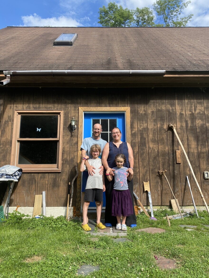 A family of four stands in front of a brown building.