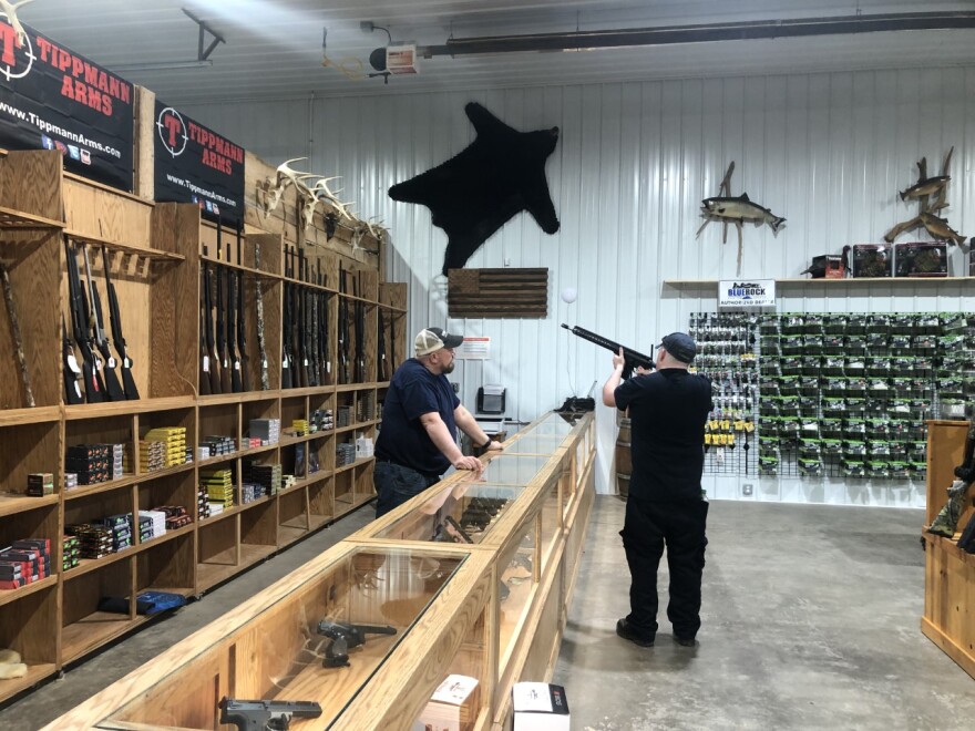 Mike Linscott (left), owner of River’s Edge Outfitters, watches as a worker examines one of the stores guns.