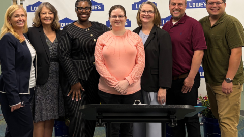 A group of people smiling in front of a Lowe's backdrop.
