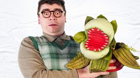 A person in glasses looking shocked with a plant puppet in one hand