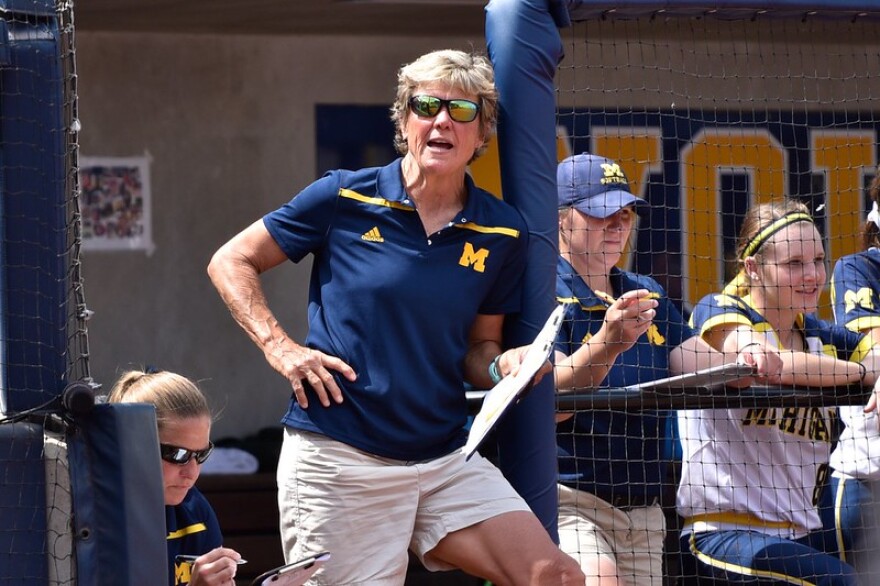 carol hutchins holds a clipboard in front of a dugout 