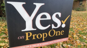 A close up of a political yard sign promoting the prop 1 ballot initiative, on a lawn strewn with fall leaves
