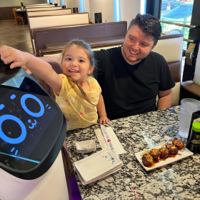 Four-year-old Emily Escalante, tickles the ears of Bella the cat robot, before eating dinner at Ninza Sushi East.