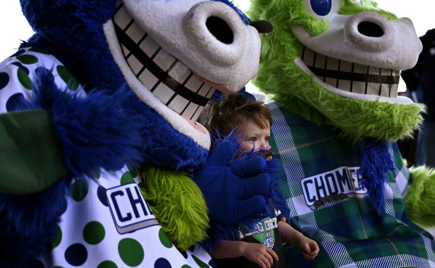 Two-year-old Rory Green of Wethersfield looks out from between mascots Chew Chew and Chompers while posing for a picture before the Hartford Yard Goats take on the Portland Sea Dogs at Dunkin' Donuts Park in Hartford for the home opener on May 11, 2021.