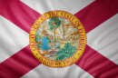 3d rendering of a detailed Florida flag, whihc is white, with red stripes coming down from the corners into an x pattern. The seal in the middle is yellow on the outside rim and says great seal of this state of florida, in god we trust. The illustration inside shows a woman in a long blue skirt depositing red and white followers into the water. There's a ship and palm tree in the background. 