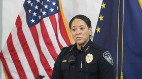 a woman speaks in front of two flags