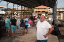 A man in a white shirt stands in front of a group of neighbors gathered for a fish fry