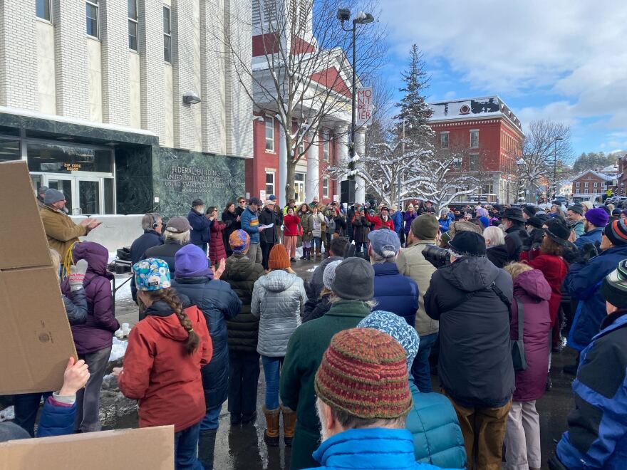 A large group of people stand outside of the Federal Building to watch speakers.