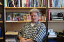 A man sits in front of a bookshelf full of textbooks and photos and smiles. 