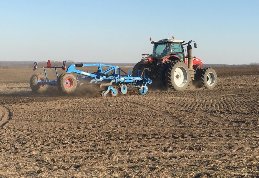 A red tractor hauls a blue, metal-framed planter across a brown, barren field that's criss-crossed with tire marks. 