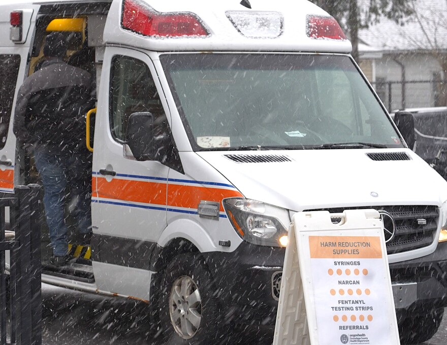 Person at the side of a van with opioid and drug harm reduction supplies, syringes, Narcan, fentanyl testing strips.