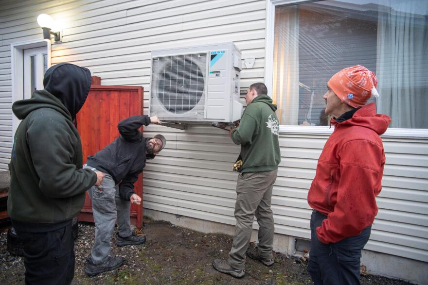 Alaska Heat Smart Executive Director Andy Romanoff, right, looks on as three Alaska Plumbing and Heating employees (from left) Cody Galletes, Sonny Ashby and Robby Brian, secure an energy-efficient heat pump onto the side of a home in Juneau.