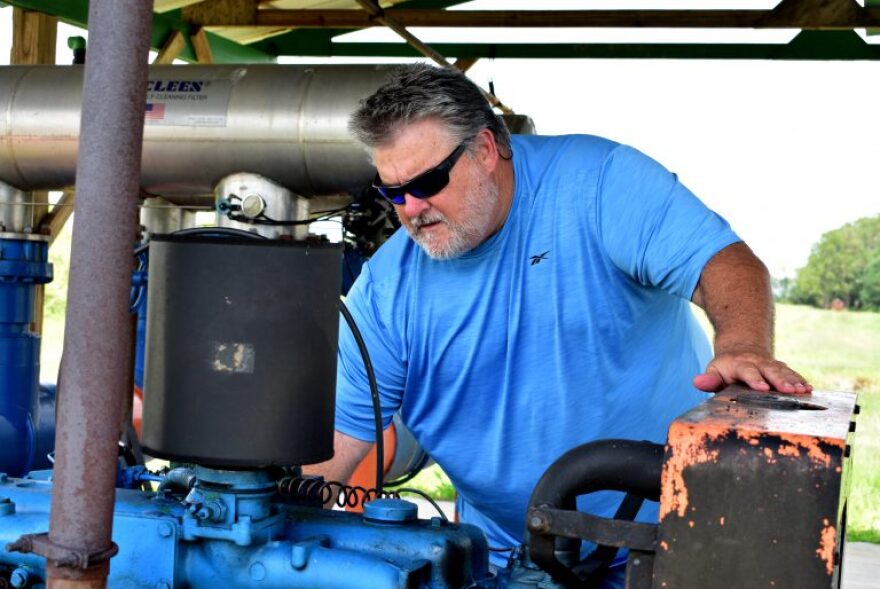 Brantley Schirard Jr. working on a machine in a grassy field.