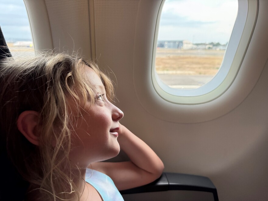 A young girl smiles as she gazes out of an airplane window.