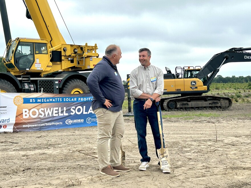 Skelton and Casper stand with shovels in front of a bulldozer and a sign for Boswell Solar