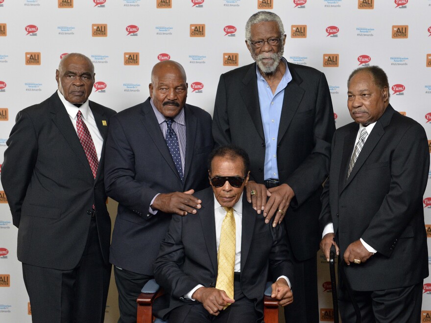 In this Sept. 27, 2014, file photo, back row from left, John Wooten, Jim Brown, Bill Russell, and Bobby Mitchell stand behind Muhammad Ali. In 1967, all five of these men attended "The Cleveland Summit," an event organized by Brown. It brought together prominent Black athletes of the time as a show of support for Ali, who faced charges after he refused to join the military during the Vietnam War.