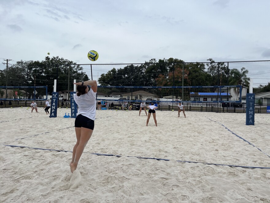a beach volleyball players about to serve a ball over the net, with two other players waiting on the other side to receive it