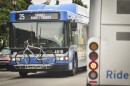 The front of a blue bus travels toward the camera on a city street.  On the front, the route marquis reads "25 Troost 83rd and Troost."