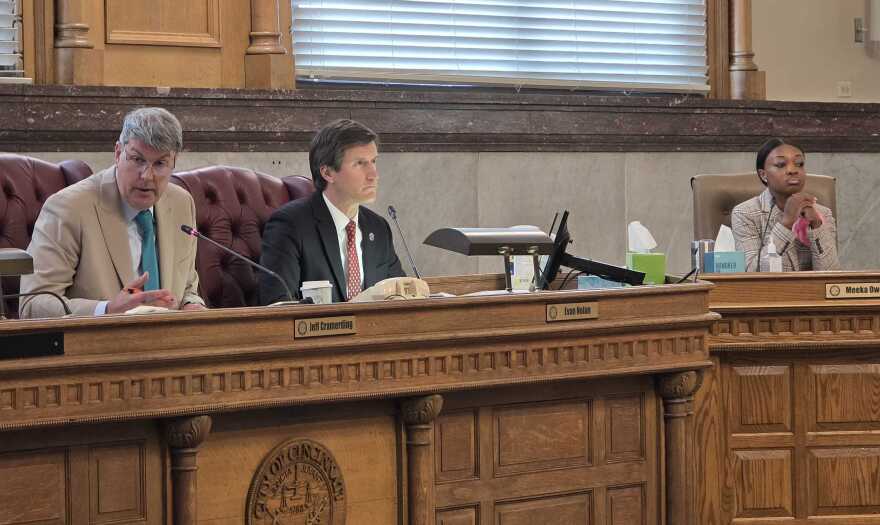 Three people sit behind a wooden dais 