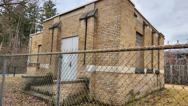 A tan, brick building surrounded by a chain link fence. 