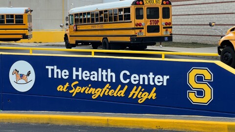 A sign announces the Health Center at Springfield High. Yellow school buses line up behind it.