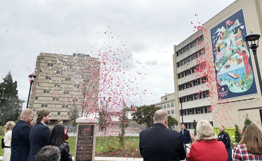 A crowd watches as red and white confetti falls in front of a campus building featuring a large mural for Bradley University.