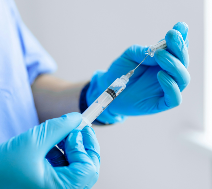 A health practictioner, mostly off-camera, fills a syringe with clear liquid.