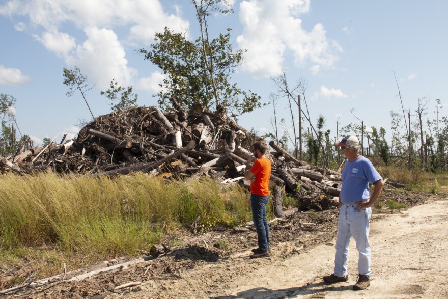 Two men stand on a dirt road and look in dismay at a pile of broken timber logs.