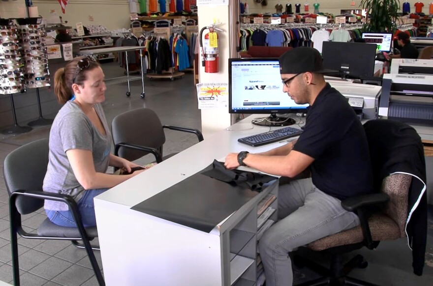 Christopher Avila, a National Guardsman, works with a customer in March during a shift at T-Shirt Mart in Point Loma, Calif. He says he lost an IT job because the guard needed him for two straight weekends, followed quickly by two weeks of training on new equipment.