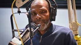  A man wearing a blue shirt talks at a microphone inside a radio studio.