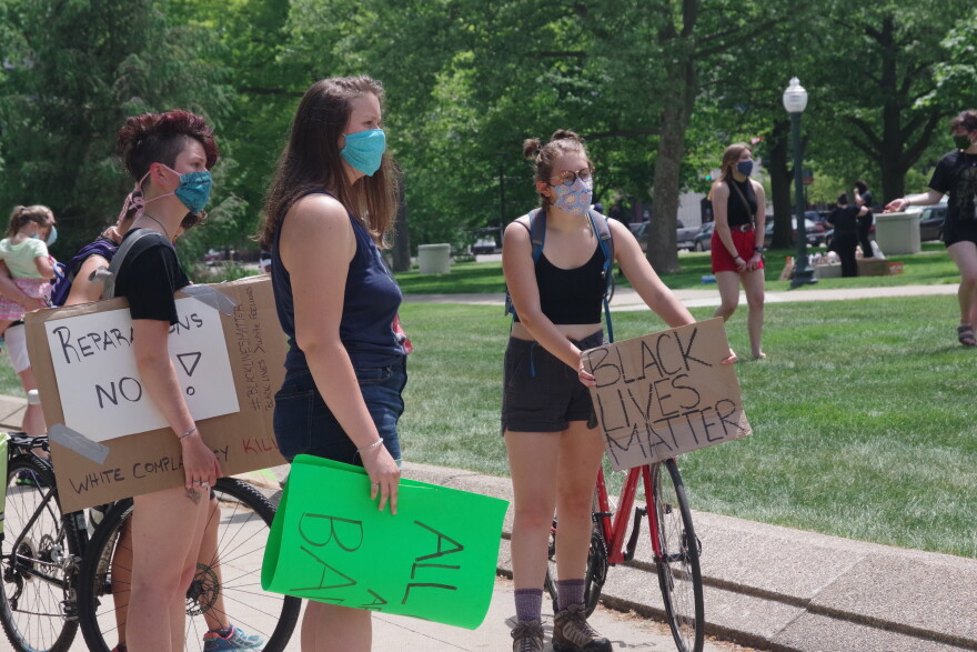 The photo shows several young woman holding signs and wearing face masks. One is also walking a red bicycle.
