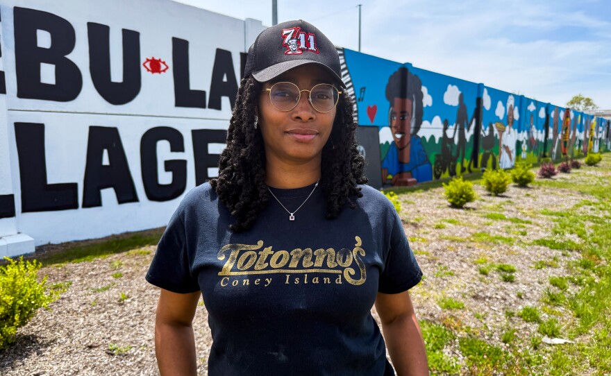 Brittany March, chef/owner of It's Food Detroit, stands in front of a mural featuring the faces of Alkebu-lan Village. Alkebu-lan offers a wide range of youth programming. March borrows Alkebu-lan's kitchen and dining space, and provides culinary training to some of the older kids in return.