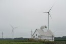 a white barn sits in a grass field surrounded by large wind turbines
