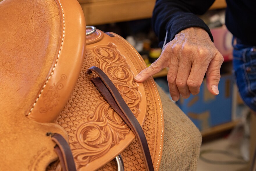 A pinky finger pointing at a section of the design on a leather saddle.
