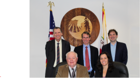 Five people in front of a county seal, the American flag, and the California flag.