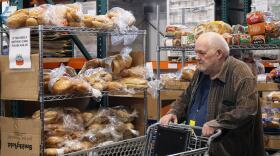 Richard Beveo pushes a shopping cart through the Cache Community Food Pantry. Behind him are shelves stocked with bread. 