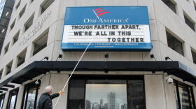 A man adjusts the One America sign in downtown Indianapolis in late March 2020. It usually displays a pun, but the message reads: "Although farther apart, we're all in this together."