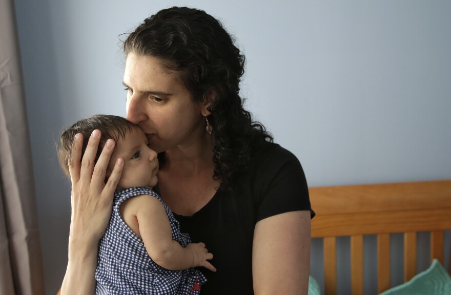 In this Thursday, June 1, 2017 photo Elena Tenenbaum kisses her eight-week-old baby Zoe while standing for a photograph at their home in Providence, R.I. Tenenbaum, a clinical psychology researcher, had her second daughter in April of 2017, and has been able to use Rhode Island's paid family leave program, which started in 2014 and covers four weeks of partial pay.