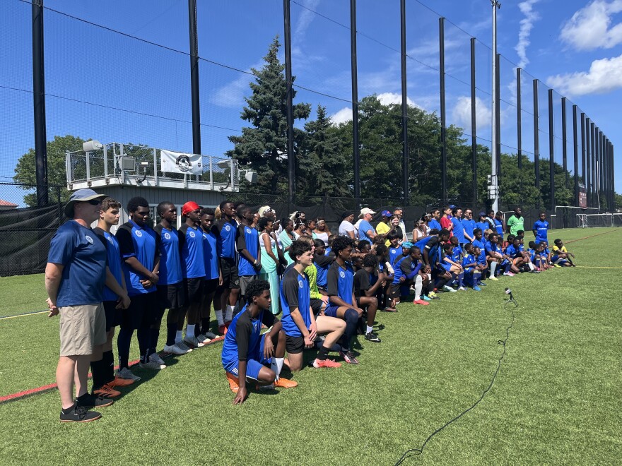 Dozens of soccer players are lined up and posing for a photo on a soccer field. 
