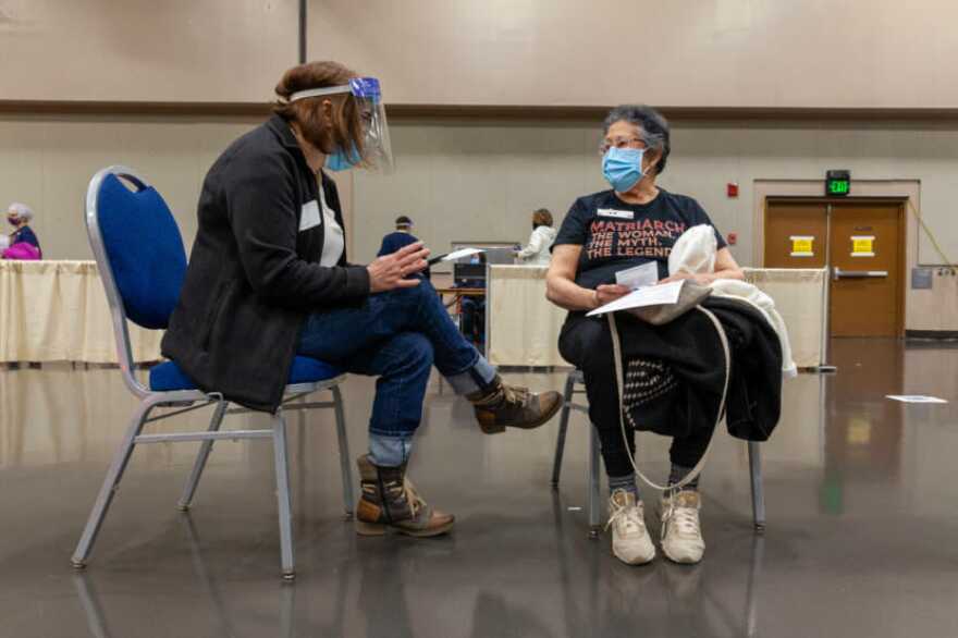 Two people in PPE sit in chairs next to aone another
