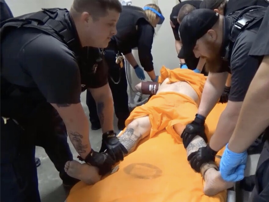 A screenshot from a video of officers at the U.S. penitentiary in Thomson, Ill., holding an incarcerated person in a four-point restraint, where both wrists and ankles are secured to restrict movement.