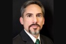 Head shot of man with a goatee and wearing a black suit with green spotted tie 