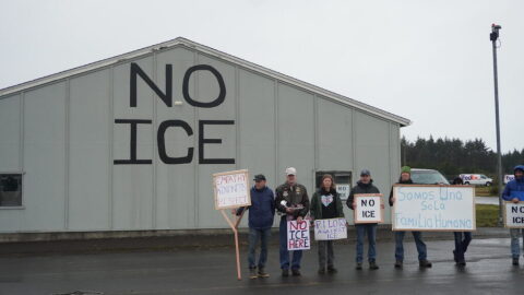 A group of local pilots and organizers stand by a hangar they have painted with “NO ICE”. “We are one human family,” a sign in Spanish held by one demonstrator reads.