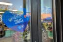 A blue sign on a shop window asks people to "shop small."