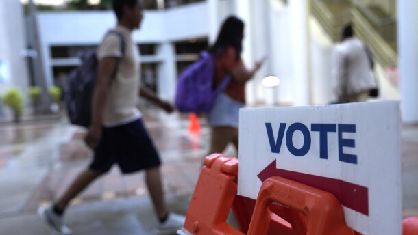 People walk past a Vote sign. 
