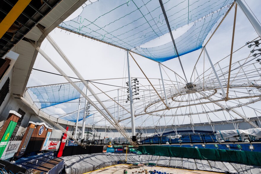 A view of the roof of Tropicana Field. There are nets over some parts of the open roof that will serve as the workers' platform. There is construction happening on the floor of the field. 