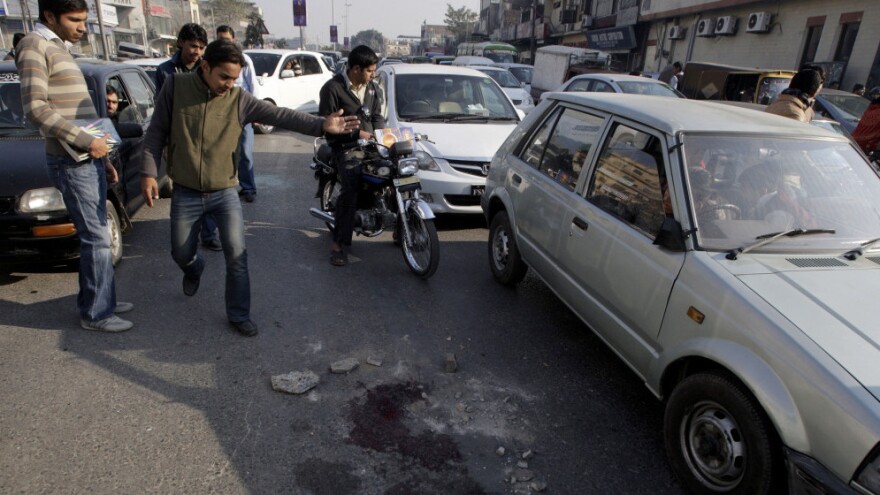 People look at blood stains on the road in Lahore, Pakistan, today (Jan. 27, 2011), where an American shot and killed two Pakistanis.