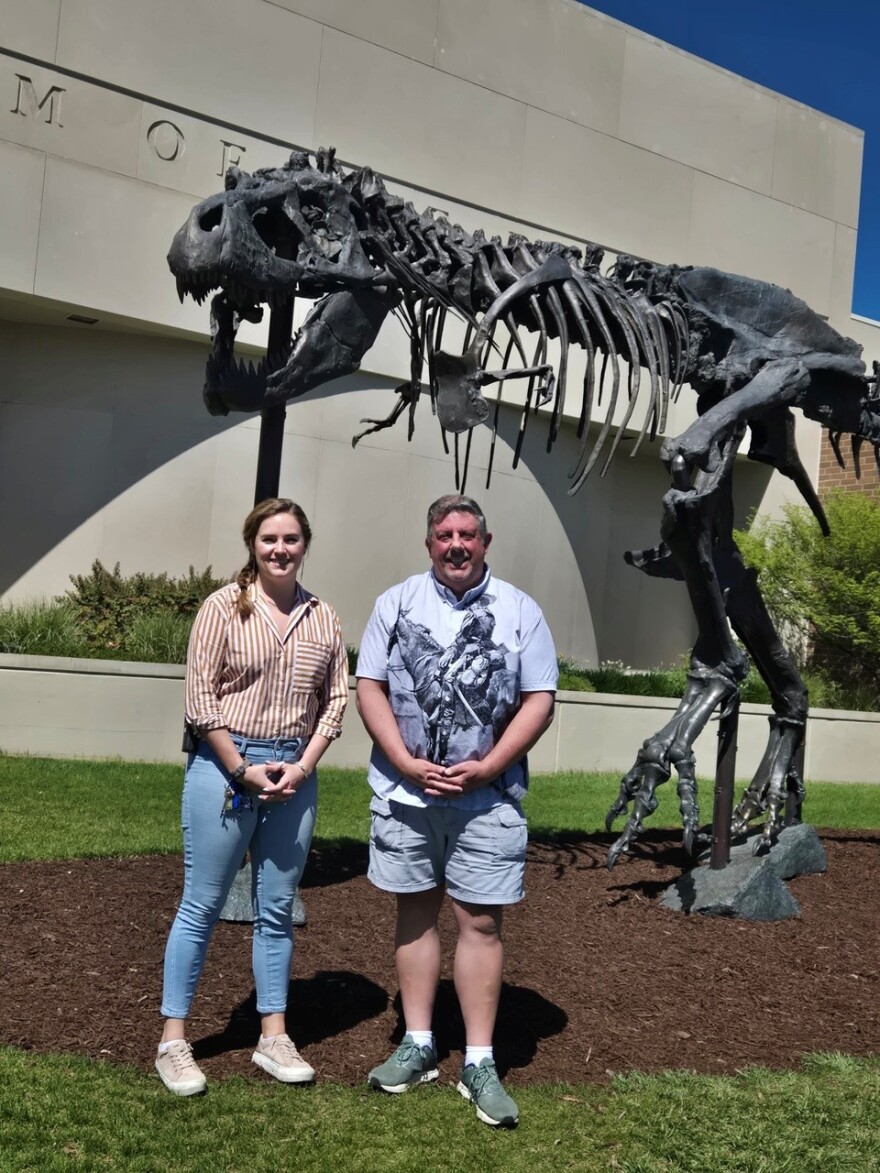 Kate Hodge (left), Director of Education and Public Programming, and Scott Williams, Senior Director of Exhibitions and Planetarium at Museum of the Rockies, stand in front of Big Mike, the bronze T-Rex statue that welcomes visitors to the museum.
