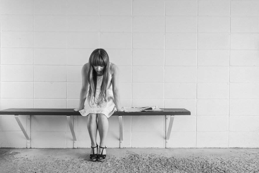 A women sitting on a bench by herself. She is looking down at the ground.