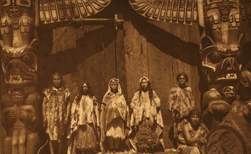 The original caption reads: "The [Kwakiutl] bride stands in the middle between two dancers hired for the occasion. Her father is at the left, and the bridegroom's father at the right behind a man who presides over the box-drum."